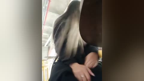 Video of a person with long, dark hair wearing a black outfit, hugging a smaller person with short, light brown hair, in a dimly lit room with exposed pipes and yellow furniture.