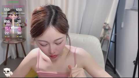 Video of an Asian woman with fair skin and dark hair, wearing a pink tank top, eating ice cream in a modern, white room.