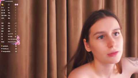 Video of a young woman with light skin, brown hair, and blue eyes, wearing a red lipstick, set against brown curtains. A digital calendar overlay shows dates and events.