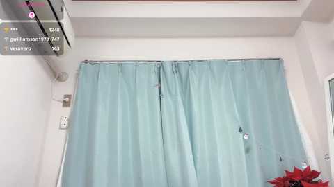 Video of a hospital room with a torn, light blue curtain covering a window, revealing a red Christmas wreath outside. The room is clean and sterile, with a white ceiling and wall.