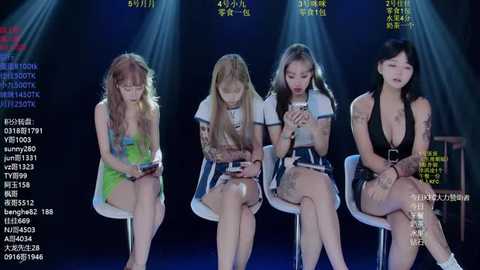 Video of four young Asian women with varying hairstyles and outfits, sitting in a dimly lit room with spotlights, appearing focused on their smartphones.