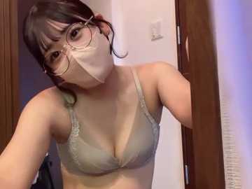 Video of a young Asian woman with light skin and dark hair, wearing a beige bra, gold-rimmed glasses, and a face mask, leaning forward in a bathroom with wooden doors.