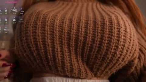 Media: Video of a close-up of a woman's large, round, brown-knit sweater, revealing a full chest. She has long, dark hair and wears a white undershirt.