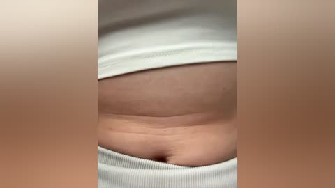 Video of a close-up, side view of a person's belly, showing natural skin folds and texture, wearing a white ribbed tank top. The background is blurred, focusing attention on the body.
