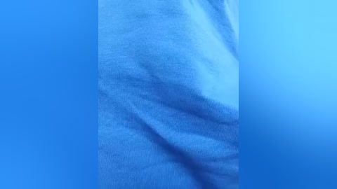 Video of a single, loose-fitting, light blue t-shirt draped over a flat surface, showcasing soft, crumpled fabric with subtle texture and natural light shadows. The background is a solid, deep blue, emphasizing the garment's color and texture.