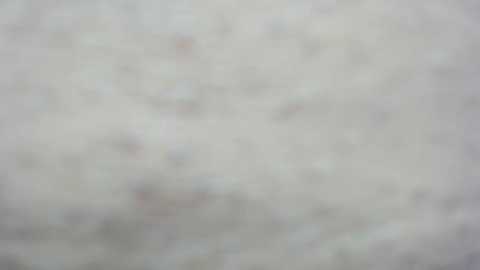 A blurry video of a white, textured surface with faint, indistinct patterns and colors, possibly snow or a light-colored fabric, giving a soft, muted appearance.