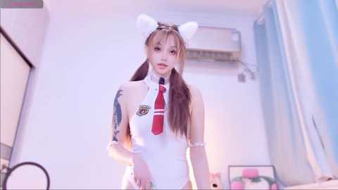 Video of an East Asian woman in a white, high-neck, sleeveless leotard with a red tie, white cat ears, and a blue ribbon on her thigh. She stands in a minimalist bedroom with a blue curtain and an air conditioner.
