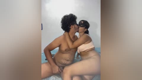 A video captures an intimate moment between a nude Black man with curly hair and a nude Latina woman with long dark hair, both with medium builds, kissing passionately.