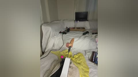 A video showing a disheveled bedroom with a messy bed, a black computer monitor on a table, and a person lying on the bed with a white cane, holding a pink object.
