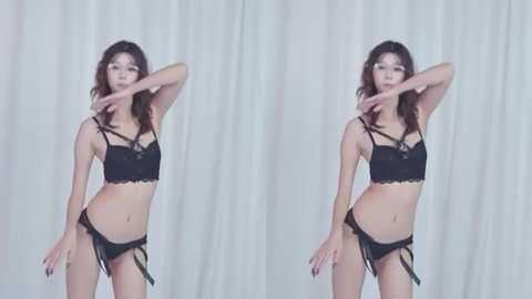 Video of a slender Asian woman with long brown hair, wearing black lace lingerie and garter belt, posing seductively against a white curtain backdrop.