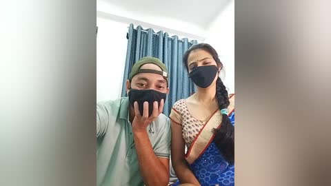 Media: Video of a man and woman in a room, both wearing black masks, the woman with a braided ponytail.