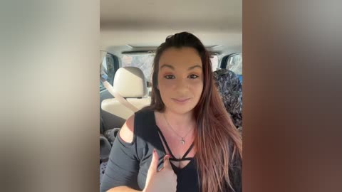 Video of a young woman with long brown hair, wearing a black off-shoulder top, smiling from the backseat of a car.