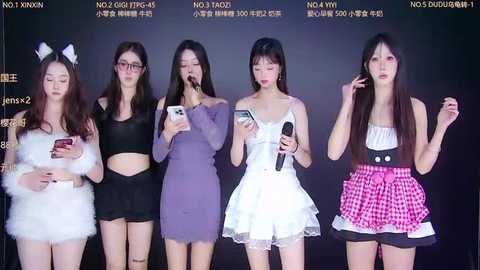Video of five young Asian women in different outfits (furry, purple, white, black, and plaid) holding phones, against a dark background with text.