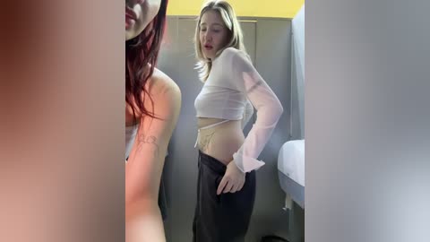 Video of two young women in a locker room, one with red hair, the other with blonde, both topless, wearing only bras and pants.