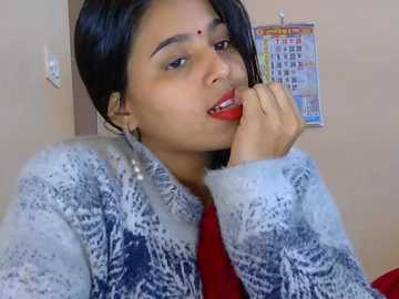 Video of a young woman with medium brown skin and straight black hair, wearing a white and blue patterned sweater, resting her chin on her hand. Background shows a calendar and beige wall.