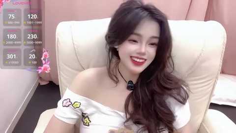 Video of a young East Asian woman with long dark hair, fair skin, and red lipstick, smiling in a white off-shoulder top with floral embroidery, sitting on a beige leather couch, with a virtual overlay showing 175 viewers.