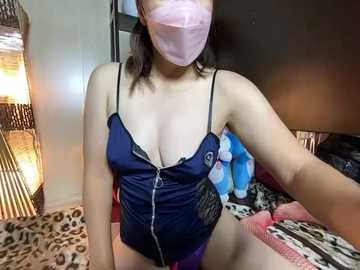 Video of an East Asian woman in a dark blue, low-cut, lace-trimmed top, revealing cleavage. She wears a pink face mask, purple panties, and is seated on a bed with leopard-print bedding.