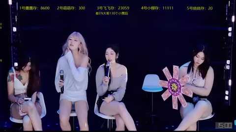 Video of four Asian women on stage, two holding microphones, one with a white dress, another with a floral dress, singing under dim lights.