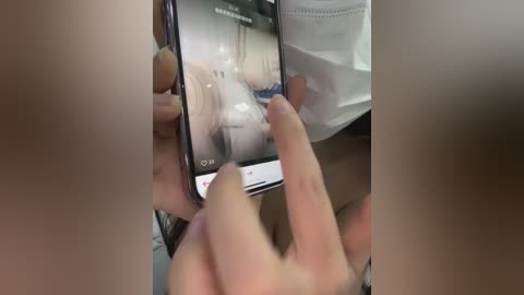 A video shows a person wearing a face mask, holding a smartphone displaying an image of a person in a white dress, with blurred background.