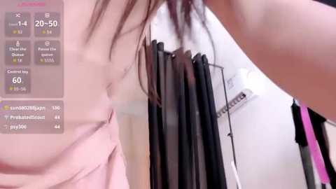 A video of a woman with long, straight brown hair in a pink dress, standing in a bathroom with a shower curtain and a digital clock displaying 20:50.