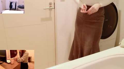Video of a person in a brown skirt, standing near a white door with a laundry machine visible. The background shows a small inset image of a person in a striped shirt working at a desk.