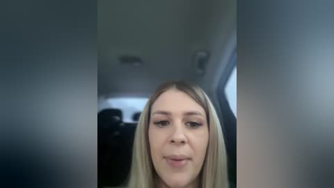 A blurry video of a blonde woman in a car, likely a selfie, with a blurred background and a dimly lit interior.
