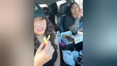 Video: Two women in a car; one eating a fried chicken leg, the other with glasses, holding a cup, tattoos on arm.