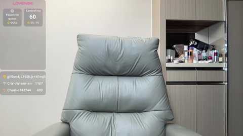 Media: Video of a modern, light gray leather recliner chair in a minimalist living room with a kitchenette in the background.