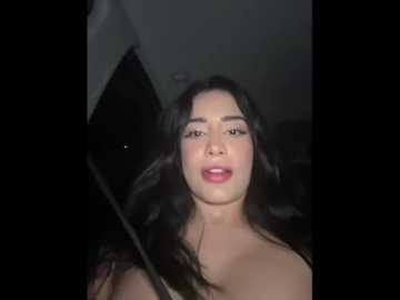 Video of a young woman with long, dark hair and fair skin, wearing a pink dress, captured indoors with dim lighting.