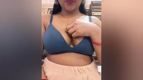 Media: A video of a light-skinned woman with medium-length black hair, wearing a blue bra and beige shorts, taken indoors with a blurred background.