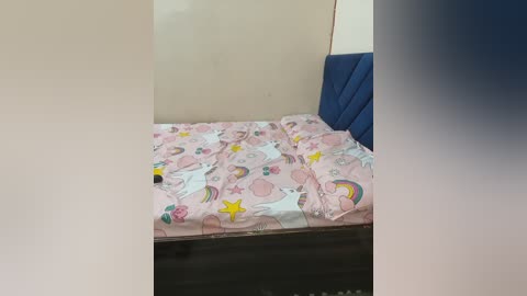 A video of a small, neatly made bed with pastel-colored unicorn-themed bedding in a simple, sparse bedroom with a dark wooden floor and blue headboard.