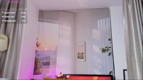 A video of a cozy bedroom with a large, partially see-through window displaying a serene sunset landscape. Soft, light-colored curtains frame the window, and a potted plant adds a touch of greenery. The room features a mix of modern and minimalist decor.