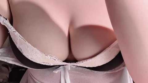 A close-up video of a woman's cleavage in a white lace bra with black straps. Her skin is fair and smooth. The background is indistinct.