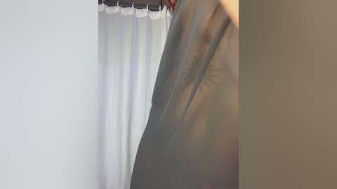 Video of a nude woman with medium skin tone, holding a white shower curtain, revealing her armpit hair. The background is a plain white wall and beige door, capturing a candid, intimate moment.