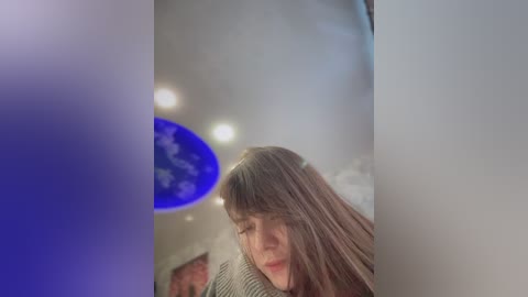 A video of a young woman with long brown hair, wearing a green sweater, hugging a blue globe in a dimly lit room. The blurred background features a blue light and a soft, diffuse light source.