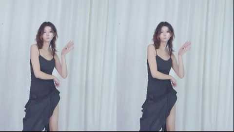Media: Video of an East Asian woman with shoulder-length brown hair, wearing a black, sleeveless, ruffled dress with a high slit, posing in front of white, textured curtains.