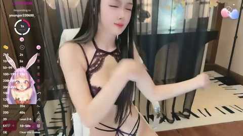 Media: Video of an Asian woman with long black hair, wearing a black lace bralette and thong, adjusting her underwear in a bedroom with black curtains and a white chair.