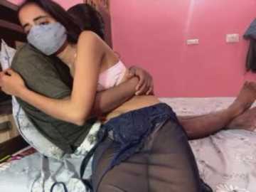 Video of a woman in a pink bra and blue skirt hugging a man on a bed with pink walls.