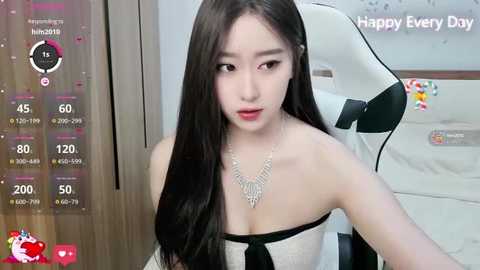 Video of an Asian woman with long black hair, fair skin, and red lipstick, wearing a strapless dress with a black bow, seated in a white gaming chair with a Happy Every Day poster in the background.