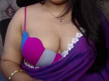 Media: Video of a woman with medium skin tone, wearing a colorful bra with pink and blue cups, a purple sari draped over her shoulders, and a gold bracelet on her wrist.