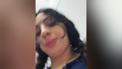 Video of a smiling woman with curly black hair, wearing a blue shirt, captured from a low angle, with blurred background.