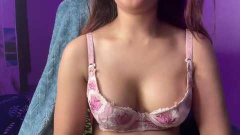 Video of a young Asian woman with light skin, wearing a pink floral lace bra, sitting on a blue towel.