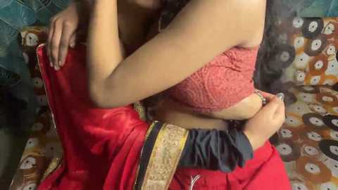 Video of a woman in a red sari, cradling a baby in a red blanket, on a colorful, patterned couch.