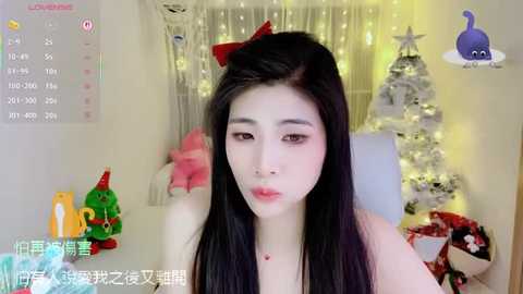 Media: A video of an Asian woman with long black hair, wearing a red bow, making a kissy face in a festive, decorated room with a Christmas tree and holiday-themed toys.