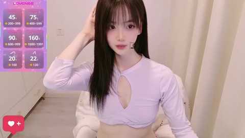 Video of an East Asian woman with straight black hair, fair skin, and a slender physique, wearing a white crop top and sitting on a bed, with a digital health tracker overlay.