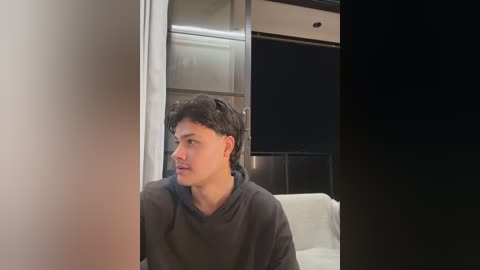 Video of a young man with short dark hair, wearing a black shirt, gazing thoughtfully into a mirrored closet door, in a modern, minimalist room with black and white decor.