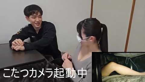 Video of a smiling Asian man in a black uniform and a woman in a gray top and face mask, seated at a table. Text overlay in Japanese.