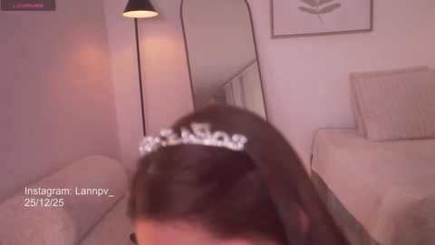 Video of a person with dark hair wearing a sparkling tiara, lying on a beige sofa in a dimly lit room.