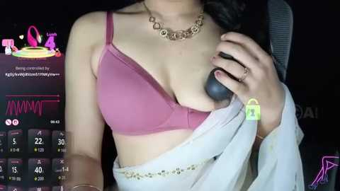 A video of a light-skinned woman with medium-sized breasts, wearing a pink bra and a white skirt, holding a microphone, against a dark background with a pink and purple digital overlay.