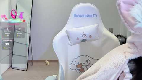 Video of a white gaming chair with a plush pillow, featuring a cartoon dog design, and a person in a plush, white bathrobe in a minimalist room with a glass cabinet showcasing colorful toys.
